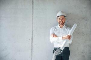 Leaning on the wall.. Holding paper with project plan. Man is working on the construction site at daytime photo