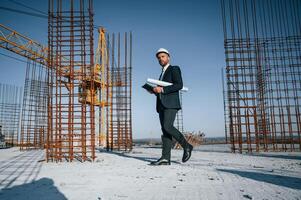 Holding paper, with plan and tablet. Businessman in formal clothes is on the construction site at daytime photo