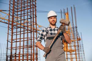 With big hammer in hands. Man is working on the ,construction site at daytime photo
