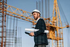 Side view,. Walking ,and holding paper with plan and digital tablet. Businessman in formal clothes is on the construction site photo