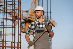 With big hammer, in hands. Man is working on the ,construction site at daytime photo