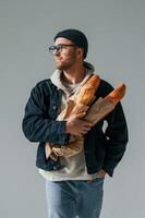 With, bunch of baguettes in hands. Handsome man is in the studio against white background photo