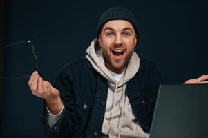Happy man is in the studio against background. Smiling, celebrating succes. Using laptop photo