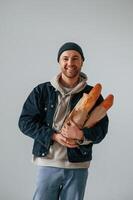 Man in hat is holding baguettes. Guy is in the,, studio against white background photo