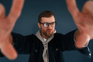 Guy is, pretending that he's doing photoshoot by using hands gestures. Handsome man is in the studio against blue background photo