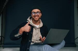 Using,,laptop and smiling. Handsome man is in the studio against background photo
