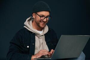 Using laptop and smiling. .Handsome man is in the studio against background photo