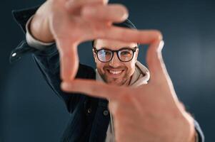 Making the photo, by hands, pretending. Smiling. Handsome man is in the studio against blue background photo