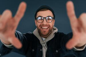 Making, the photo by hands, pretending. Smiling. Handsome man is in the studio against blue background