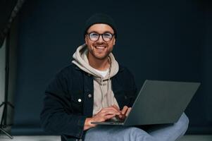 Using laptop and smiling. Handsome man ,is in the studio against background photo