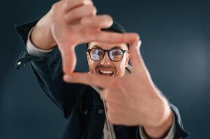 Making the photo by hands, pretending. Smiling. Handsome man is in the studio against blue background