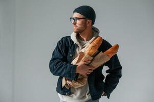 With ,,bunch of baguettes in hands. Handsome man is in the studio against white background photo