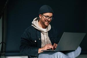 Using laptop and smiling. Handsome man is in the studio against background photo
