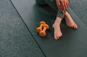 Close up view. Legs and yellow dumbbells. Young woman in yoga clothes doing fitness indoors photo
