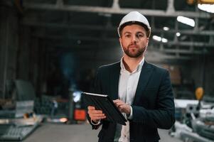 Holding black, digital tablet in hands. Manager in black formal wear at the factory photo