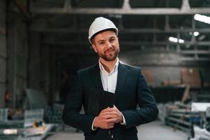 Positive manager in black formal ,wear, at the factory. Standing and smiling photo