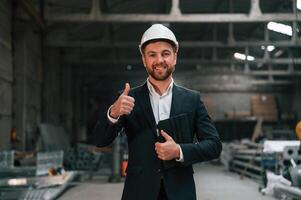 Positive,, manager in black formal wear at the factory. Standing and smiling photo