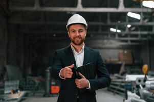 Positive manager in black formal, wear at the factory. Standing and smiling photo