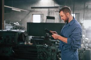 Working by, using digital tablet. Man at the factory that is in blue uniform is indoors photo