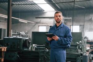 Working by using, digital tablet. Man at the factory that is in blue uniform is indoors photo