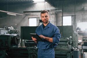 Working ,by, using digital tablet. Man at the factory that is in blue uniform is indoors photo