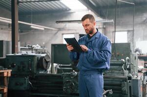 Working,, by using digital tablet. Man at the factory that is in blue uniform is indoors photo