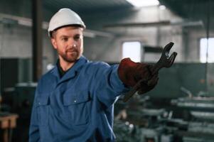Wrench in the hand... Factory worker in blue uniform is indoors photo