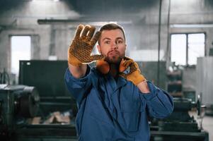 Showing stop gesture by a hand. Factory ,worker, in blue uniform is indoors photo