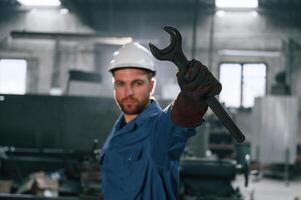 Wrench, in the hand. Factory worker in blue uniform is indoors photo