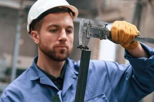 Using calliper to measure metal pipe.. Factory ,worker in blue uniform is indoors photo
