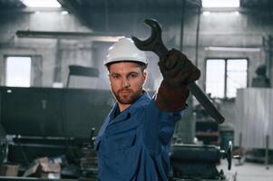 Wrench i,n the hand.. Factory worker in blue uniform is indoors photo