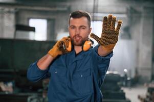 Showing stop gesture, by a hand. Factory worker in blue uniform is indoors photo