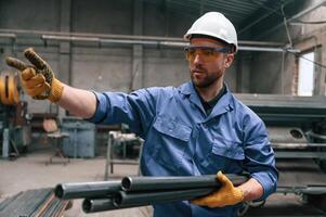Looking ,to the side and holding ,metal pipes. Factory worker in blue uniform is indoors photo