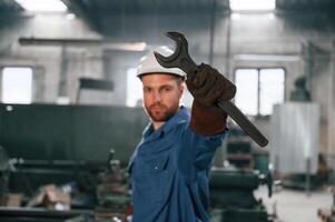 Wrench i,n the hand. Factory worker in blue uniform is indoors photo