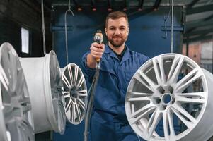 Holding paint, spray gun. Car service station, worker is taking care about disks of tires photo