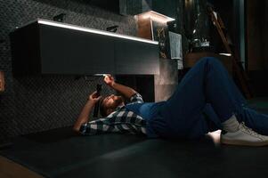 Using ,flashlight. Fixing water tap. Plumber in blue uniform is at work in the bathroom photo