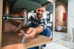 Taking a wrench. Plumber in blue uniform is at work in the bathroom photo