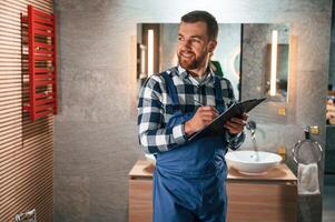 With ,notepad in, hands. Plumber in blue uniform is at work in the bathroom photo