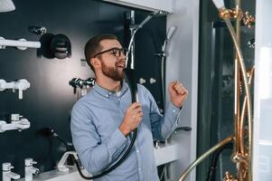 Using faucet as microphone, singing. Man chooses a products in a sanitary ware store photo