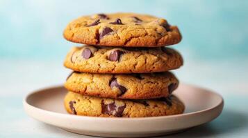 Closeup of Four Golden Brown Chocolate Chip Cookies Stacked on a Pale Pink Plate Against a Blue Background photo