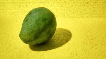 a single green mango on a yellow wall photo