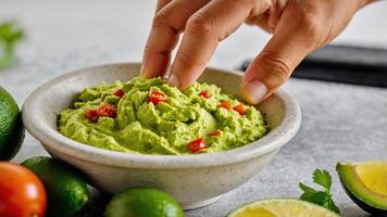 Close-up of a Hand Dipping into Freshly Made Guacamole with Tomatoes photo