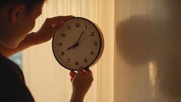 Setting Time, Man adjusting a clock on a wall in warm light, demonstrating punctuality and time management for daily schedules photo