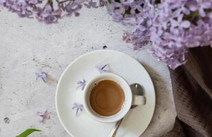 The postcard is beautiful. A fancy purple coffee mug, an old book, a straw hat and a bouquet of purple lilac. Beautiful still life. Spring time. The concept of Good morning. photo
