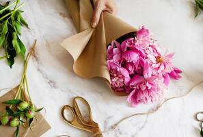 A scene depicting the creation of a floral bouquet, focusing on the beauty of pink peonies and the tools used for arranging them. photo