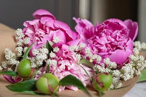 An image of someone preparing a floral gift or bouquet, surrounded by lush pink peonies, twine, and scissors on a marble surface. photo