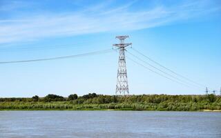 High voltage lines and power pylons in a flat and green agricultural landscape on a sunny day with cirrus clouds in the blue sky. photo