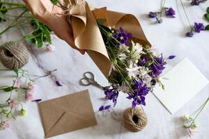 Preparing a floral gift hands arrange a bouquet of purple and white flowers, with a blank card for a personal message. photo