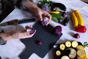 Woman cooking fresh salad with ripe red cabbage at grey table photo