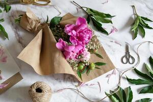 Hands working with pink peonies, scissors, and twine, creating a beautiful and natural floral arrangement. photo